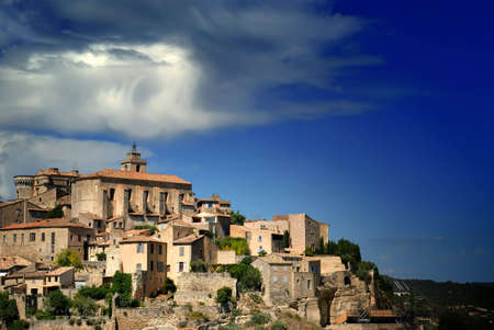 View of ancient medieval hilltop town of Gordes in France, under a dramatic, partly cloudy sky.の写真素材