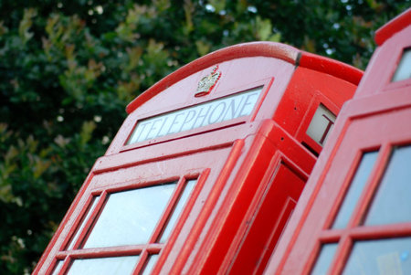 Detail of a red phone booth in London, England, with leaves in the background