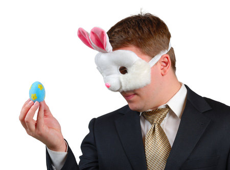 Young man wearing suit with Easter Bunny mask, looking at an Easter egg which he is holding in front...