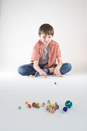 A boy plays a game of marbles. Vertical, isolated studio portrait.の写真素材