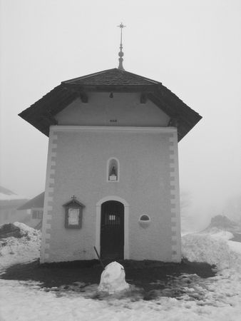A small church surrounded by snow, with a half-melted snowman in front of the entrance.の写真素材