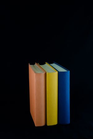 Three books,with orange, yellow and blue spines, lined up in a row. Isolated against black background.の写真素材