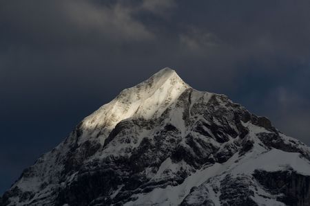 A sunbeam illuminates the peak of a tall mountain in the alps, as a darkness approachesの写真素材