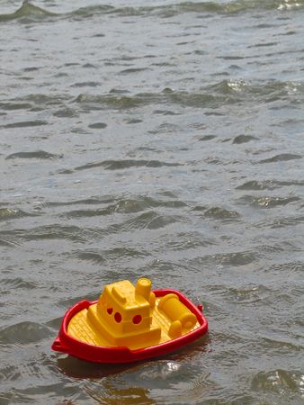 A red and yellow plastic toy fishing boat bobs in small waves in the ocean.の写真素材