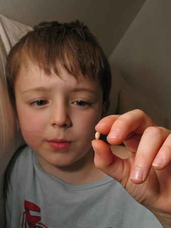 A boy holds up the tooth he just lost, visible close-up in the foreground, with traces of blood on the tooth and the boy's cheek. Vertical portrait.の写真素材
