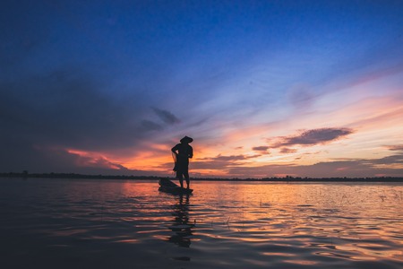 Asian fisherman on wooden boat casting a net for catching freshwater fish in natureの写真素材