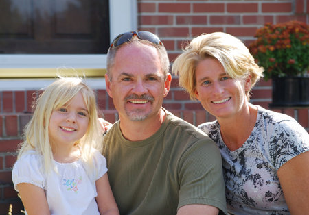 family of three posing in front of home