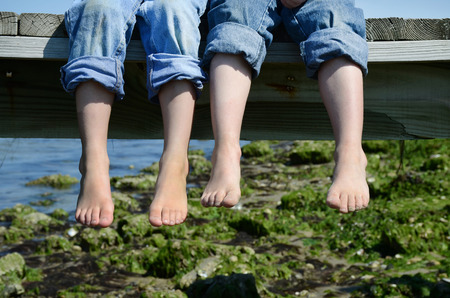 two barefoot boys in jeans sitting on dockの写真素材