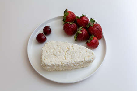 Cottage cheese with berries, strawberries, and cherries on a white round plate. On white backgroundの写真素材