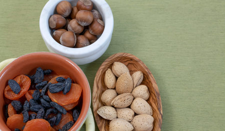 Dried fruits and nuts. Almonds and hazelnuts. In bowls against the background of a green tablecloth.