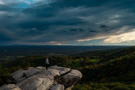 girl stand on edge of rock, aerial view of mountains, sunset light and cloudy sky, Gertrudes Nose NY