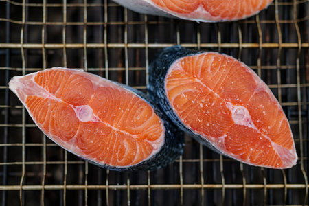 Close up of fresh salmon steak prepared for grilling with grains of salt on it, lies on grill mesh ....