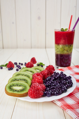 Berry smoothie.Fresh summer cocktail.Blueberry,raspberry,kiwi.Vitamin A. Vitamin C.Checkered napkin.On white wooden table with ingredients.Healthy lifestyle.Diet and weight loss concept.の写真素材