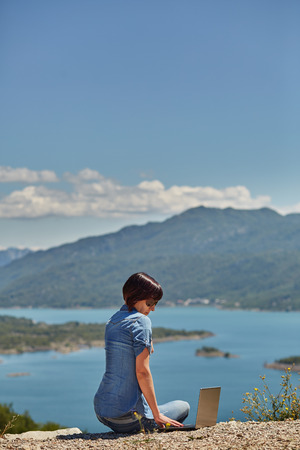 Beautiful young freelancer woman using laptop sitting on the lake.Happy smiling girl working online.Studying and learning using notebook computer.Freelance work,business people concept.の写真素材