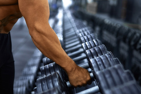 Muscular bodybuilder in gym take dumbbell from dumbbell rack.Strong athletic man naked torso working out,gaining weight. Bodybuilding concept.の写真素材