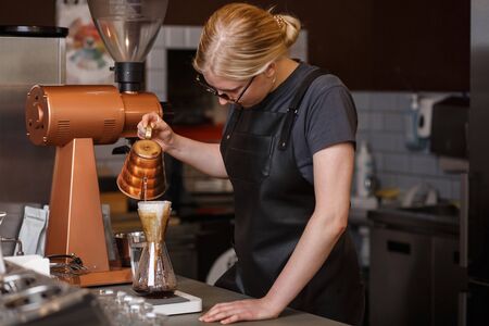 Professional barista preparing coffee using pour over coffee maker and drip kettle. Young woman making coffee. Alternative ways of brewing coffee. Coffee shop concept.の写真素材