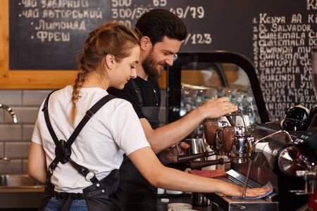 Two young smiling barista at work. Professional barista team brewing coffee using coffee machine in coffee shop. Happy young man and woman developing own coffee business. Coffee shop concept.の写真素材