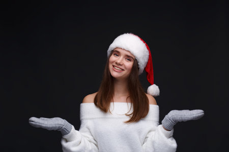 Portrait of young beautiful smiling girl in red Santa hat with white snowflakes on a dark background. Xmas fashion model with long straight hair. Winter holidays, Christmas, New Year concept.の写真素材