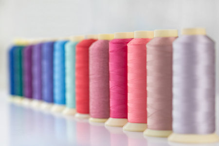 Row of multicolored spools of sewing threads on a white table. Workplace of seamstress. Sewing...