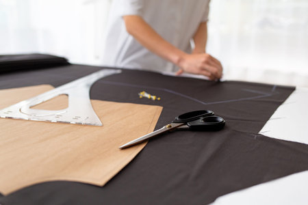 Young female dressmaker making a pattern on a piece of dark cloth. Close up portrait of fashion...