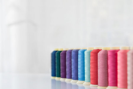 Row of multicolored spools of sewing threads on a white table. Workplace of seamstress. Sewing...