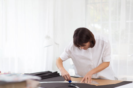 Young female dressmaker making a pattern on a piece of dark cloth. Portrait of fashion designer...