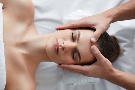 Young beautiful woman enjoying anti-aging facial massage.Male therapist making head massage to female client.Professional masseur.Relaxation,beauty,spa,body and face treatment concept.の写真素材