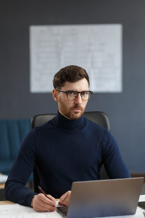 Young businessman working in office with laptop. Business portrait of handsome bearded man wearing...