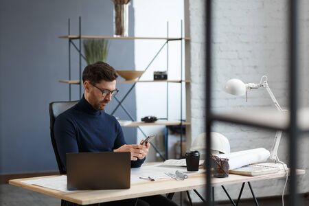 Young man using smartphone and smiling. Happy businessman using mobile phone apps, texting message, browsing internet, looking at smartphone. Concept of young people working with mobile devices.の写真素材