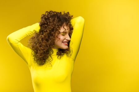 Portrait of young beautiful smiling women with curly hair. Happy girl with wavy hairstyle and bright make up isolated over yellow background. Beauty and hair care concept. Yellow lifestyle.Copy space.の写真素材