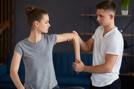 Female patient doing physical exercises with physiotherapist. Male therapist treating injured...