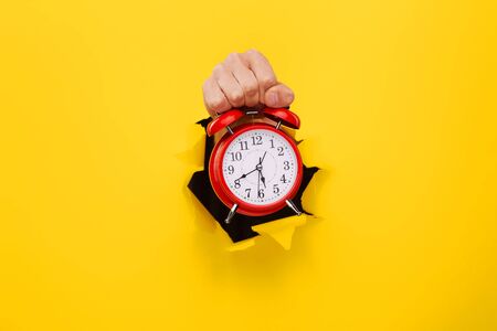Red alarm clock in a hand on a yellow background. Time concept.の写真素材