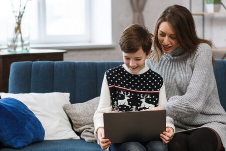 Stay home. Portrait of smiling mother and son using laptop for a online meeting, video call, video conference with relatives, home education. Happy family spending time together at home.の写真素材