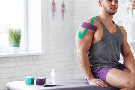 Kinesiology taping. Kinesiology tape on patient shoulder. Injured shoulder treatment of young male athlete. Post traumatic rehabilitation, sport physical therapy, recovery concept.の写真素材