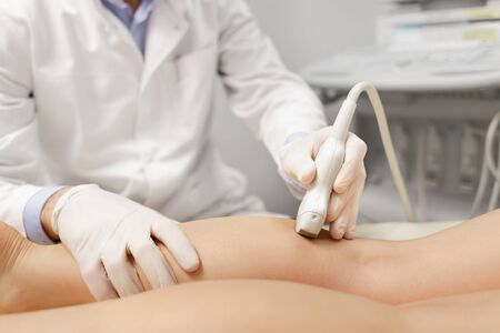 Orthopedist doctor doing ultrasound examination of patient's leg veins in his office. Young woman passing ultrasound scan in clinic. Doctor work. Medical research.の写真素材