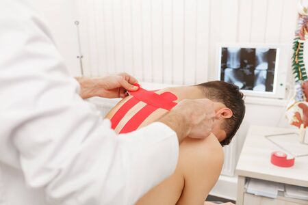 Kinesiology taping. Physical therapist applying kinesiology tape to patient neck. Therapist treating injured trapezius muscles of young athlete. Post traumatic rehabilitation, sport physical therapy.の写真素材
