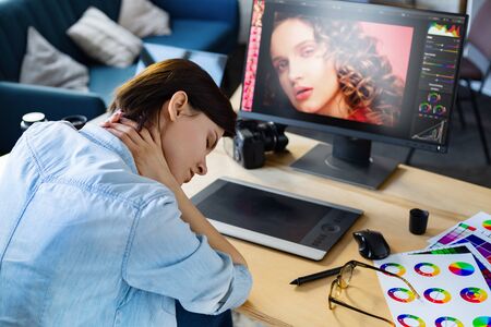 Portrait of tired graphic designer working overtime in office. Stressed worker have eye strain symptoms. Retoucher workplace in photo studio. Burnout and overwork concept. Creative agency.の写真素材