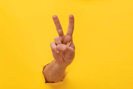 Hand on yellow trend color. Torn paper. Copy space. Victory hand.