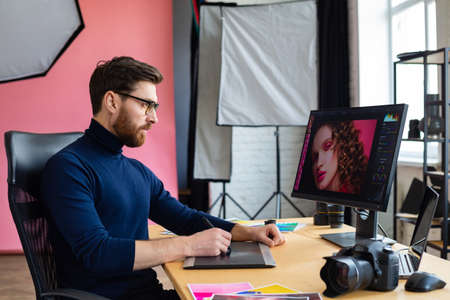 Retouching images in special program.Portrait of graphic designer working in office with laptop,monitor,graphic drawing tablet and color palette.Retoucher workplace in photo studio.Creative agency.の写真素材
