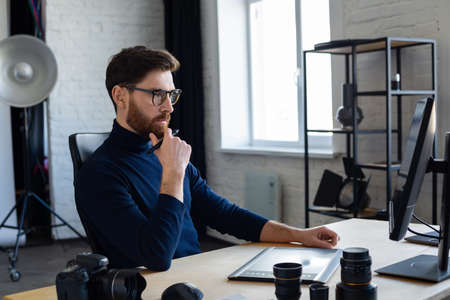 Retouching images in special program.Portrait of graphic designer working in office with laptop,monitor,graphic drawing tablet and color palette.Retoucher workplace in photo studio.Creative agency.の写真素材
