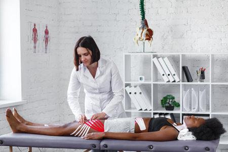 Kinesiology taping. Physiotherapist applying kinesiology tape to patient hips.Therapist treating...