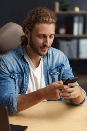 Young man using smartphone and smiling. Happy businessman using mobile phone apps, texting message,...