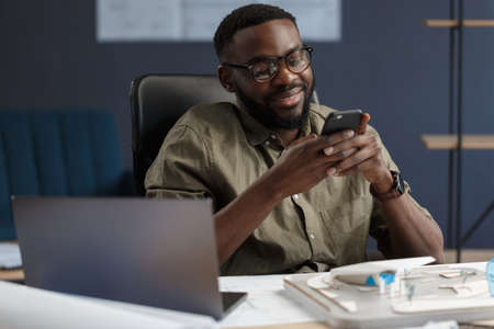 Young Afro-American man using smartphone and smiling. Happy businessman using mobile phone apps, texting message, browsing internet, looking at smartphone. Young people working with mobile devices.の写真素材