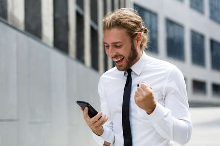 Portrait of a successful young businessman. A curly-haired man in a white shirt with a telephone against the background of a modern business center.の写真素材