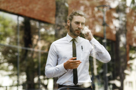 Portrait of a successful businessman who solves problems over the phone. A curly-haired manager, in a white shirt and tie, is talking excitedly on his cell phone.の写真素材