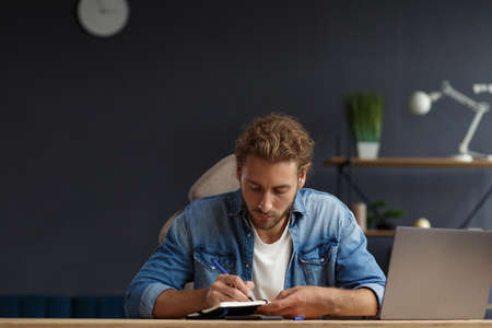 Young handsome curly smiling man with long hair studying in home with laptop.Business portrait of handsome manager sitting at workplace.の写真素材