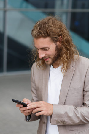 Portrait of handsome curly businessman in casual wear holding smartphone and smiling.Successful...