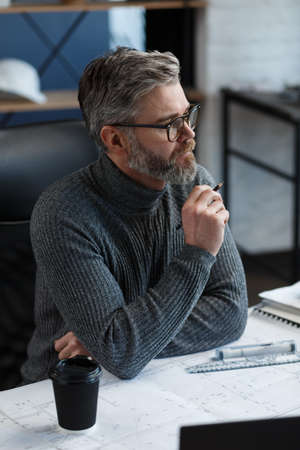 Interior designer working in office with blueprints.Engineer inspect architectural plan, sketching a construction project.Portrait of handsome bearded man at workplace. Business construction concept.の写真素材