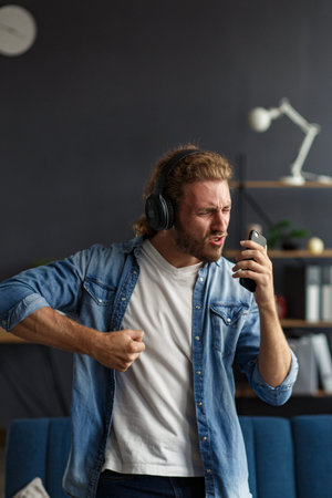 Handsome long haired curly man with headphones listening music,singing and dancing.Funny emotional...
