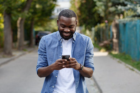 Happy man using mobile phone apps, texting message, browsing internet, looking at smartphone. Handsome Afro-American man using smartphone and smiling. Young people working with mobile devices.の写真素材